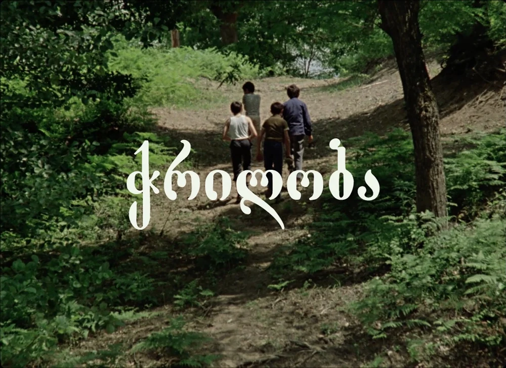 A film still of four children walking away up a wooded path, with a title in Georgian script across the frame.