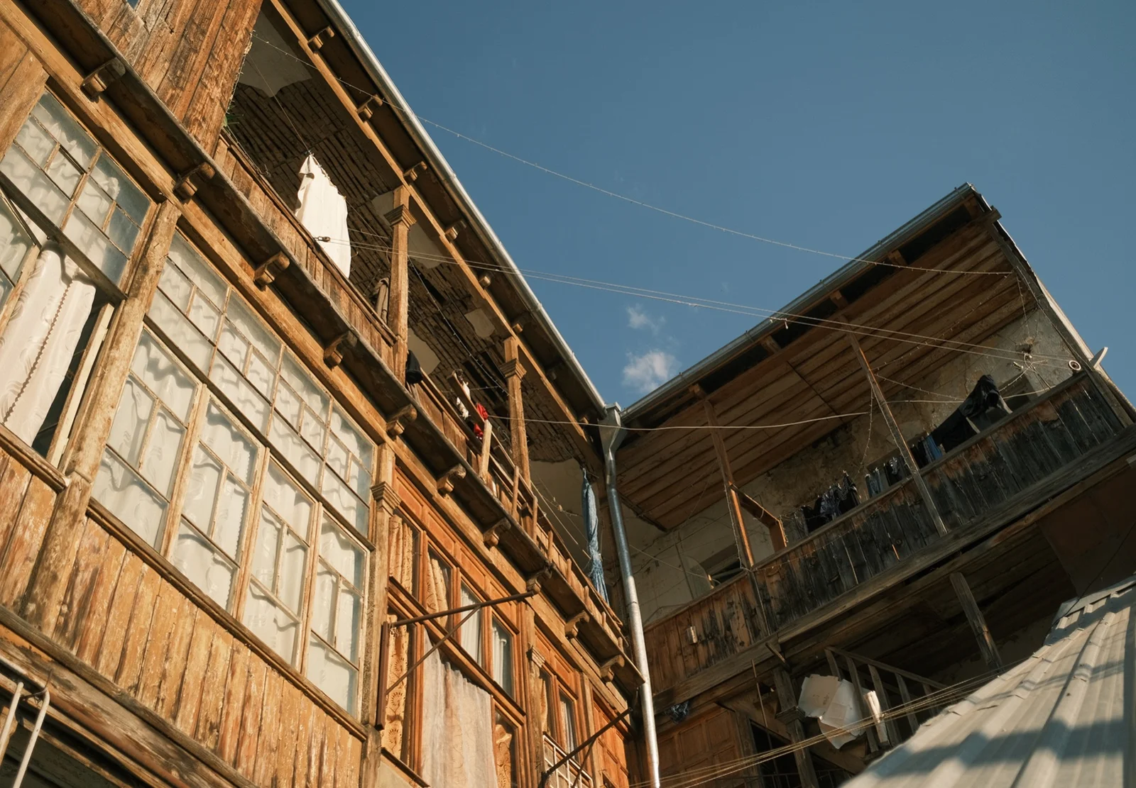 Looking up at the weathered timber balconies of a Tbilisi apartment building against a clear blue sky.
