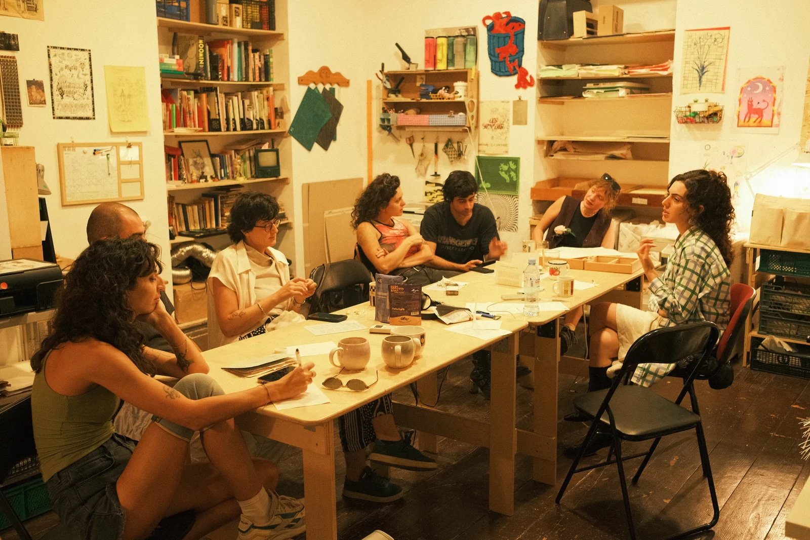 Seven people working around a large plywood table in a print studio.